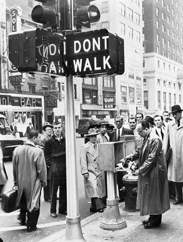 1955
In 1955, in the city of New York, the rather bulky neon "DONT WALK" and "WALK" pedestrian
signal was installed and introduced. It was manufactured by Winkomatic. In the picture, a pair
is depicted. At the time, each one was practically brand new, since both pedestrian signals
were recently installed. 

Below them is former (then) traffic commissioner Henry Barnes, in which he is depicted
as working with the newly installed signalized intersection's electro-mechanical signal controller
amidst curious fellow New Yorkers on the street.

Circa 1955 as some sources claim.
Keywords: Traffic_Lights