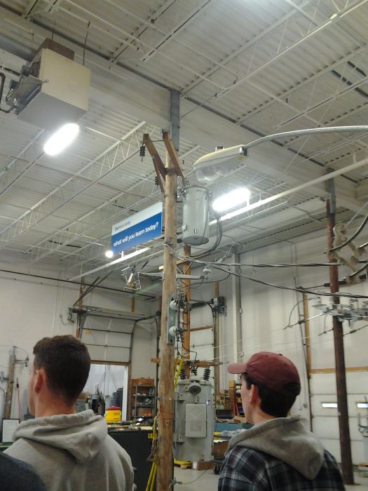 National Grid Training Facility: Regulator
On the pole in the center of the pic there's a transformer at the top of the pole and a regulator toward the bottom (though normally would be mounted toward the top of the pole; it's low down for demonstration purposes and none of it is live). The regulator regulates the voltage based on peak times and stuff. It had some cooling fins that you can barely see toward the right hand side of it. I joked that it looked like a giant coffee mug.

Also, kinda hard to see in the pic, but the top shelf of that rack just to the right of the opened bay door (look to the left of the utility pole the regulator is on) there's a big cardboard box. It's marked GENERAL (GE) ELECTRIC. Anyone wanna guess what that is? ;-)

We haven't even gotten the tour of the exterior of the facility (which parts of are indeed live; there's several street lights outside and for some reason they're all intentional dayburners, perhaps to signal that the poles are live). 
Keywords: Miscellaneous