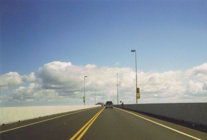 Confederation Bridge, 1997
Here's a shot of the Confederation Bridge that links together PEI and New Brunswick looking towards PEI in the summer of 1997 shortly after it opened. Note the not yet in use incandescent 12-12-12 signal heads and the fibre optic blank out speed limit signs.

I believe they were still putting some finishing touches on the bridge as in 2005 the speed limit was raised to 80 km/h. The shoeboxes are HPS, unknown wattage. 

Film scan of a 4X6 print. 
Keywords: American_Streetlights