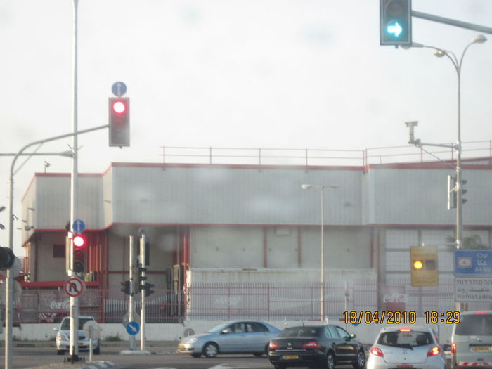 A LED traffic light system near the Carmel Tunnels.
Most of the time the right lights in this smart traffic light system are green and the left lights are red as in the photo.
The orange wig-wag flasher in the distance is also LED based and is used to prevent vehicles to stand on the railroads, that are used by a cargo trains.
You can also see the detector volume of this system in one of the lampposts that one of the traffic lights are installed. But there is also possible that this is actually a hidden camera.
Keywords: Traffic_Lights
