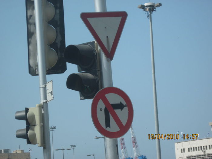 Israelis traffic signs and lights with a highmast, street lights and the floodlights of Haifa port (Harbor) in the background
The upper white triangle sign with a red square means: Give right of way.
The lower sign means: No turn (Don't turn by this arrow).
The traffic lights are all incandescent.
Most the lights in the background (Highmast lanterns and the Haifa harbor lighting) uses 400W HPS lamps except the street lights that uses european tri-band 250W MH lamps.
Keywords: Traffic_Lights