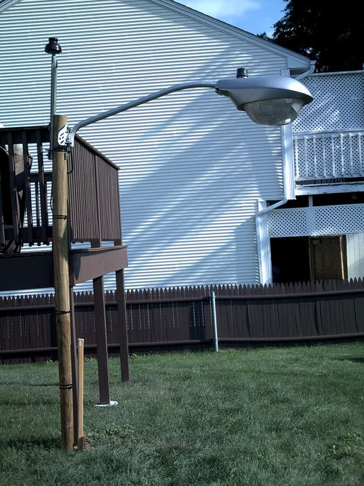 OV-25 in the Backyard!
Well, after the pic this came down and the pole is headless once again. The pole couldn't handle the weight of the OV-25 (which is about 15-20 pounds i'd guess) and was bending forward. The light was swaying violently in just a breeze and the light kept sagging more and more so i took it down before it ending up damaged. I had that bad feeling in my stomach that something was about to go wrong. BTW, this had a 300W incandescent lamp and a 120V DTL PC from 1999 that would have been used if it could stay up. 

The M-250A won't be going out back unfortunatly, since it's heavier than the OV-25. The only light that can go on the arm besides my Low Budget Area Light would be the NEMA Jace will be sending. Hopefully it's able to be on the set-up without fear of it getting damaged.
Keywords: American_Streetlights